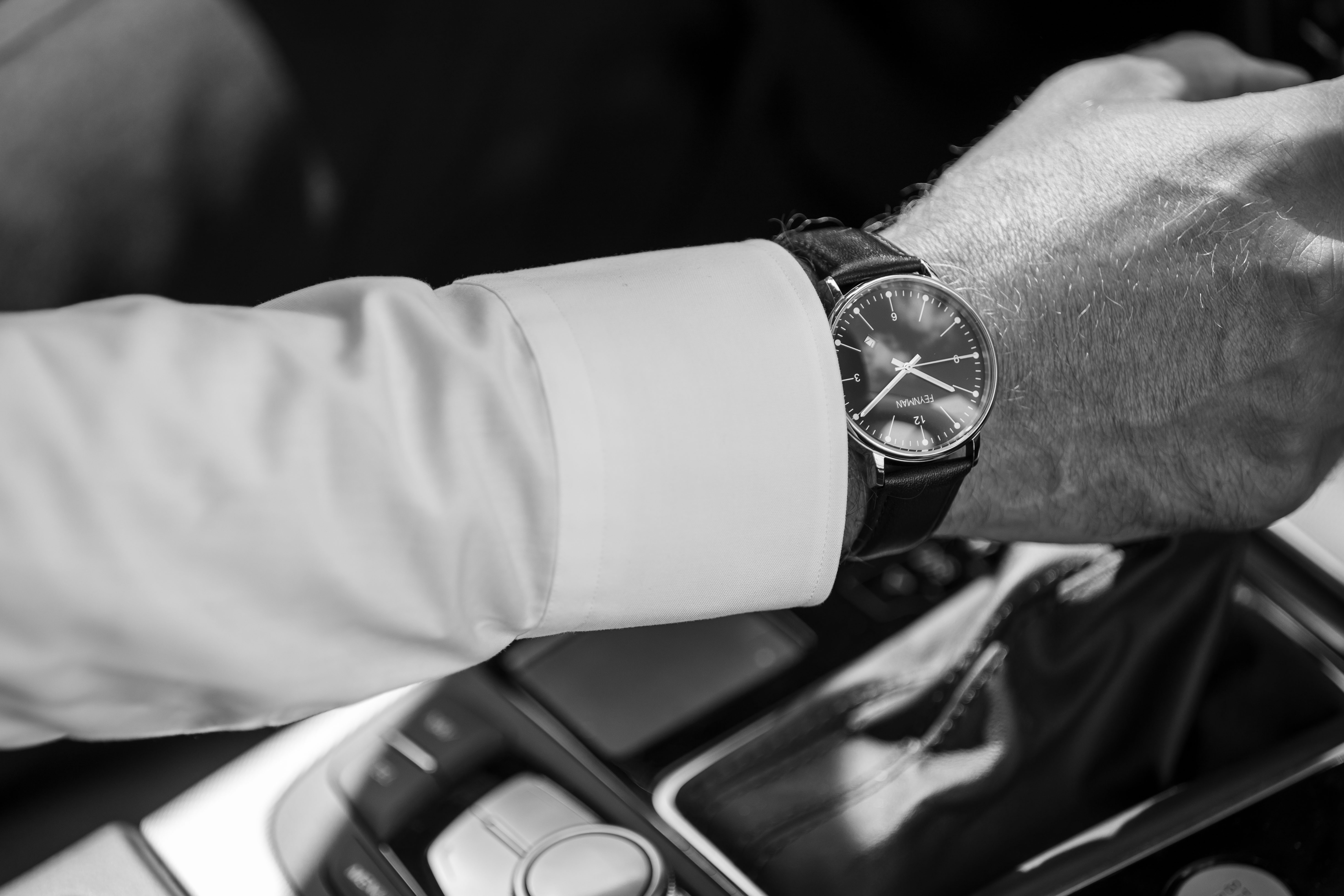 Photo of the wrist of a man, wearing a shirt and a Feynman CWII watch, in a car