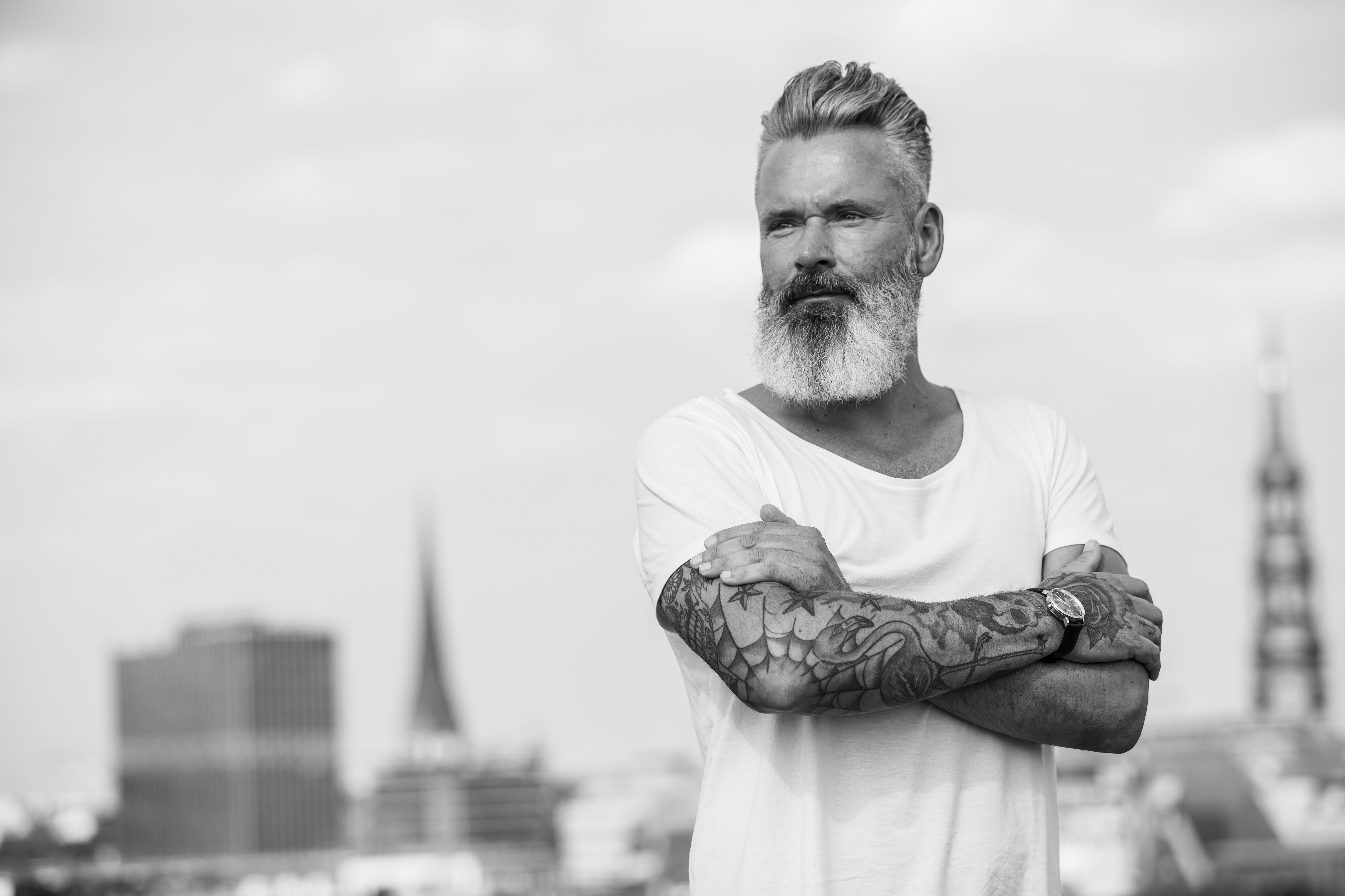 Photo of a bearded, tattooed man in a t-shirt wearing a Feynman CWII watch in front of the Hamburg skyline